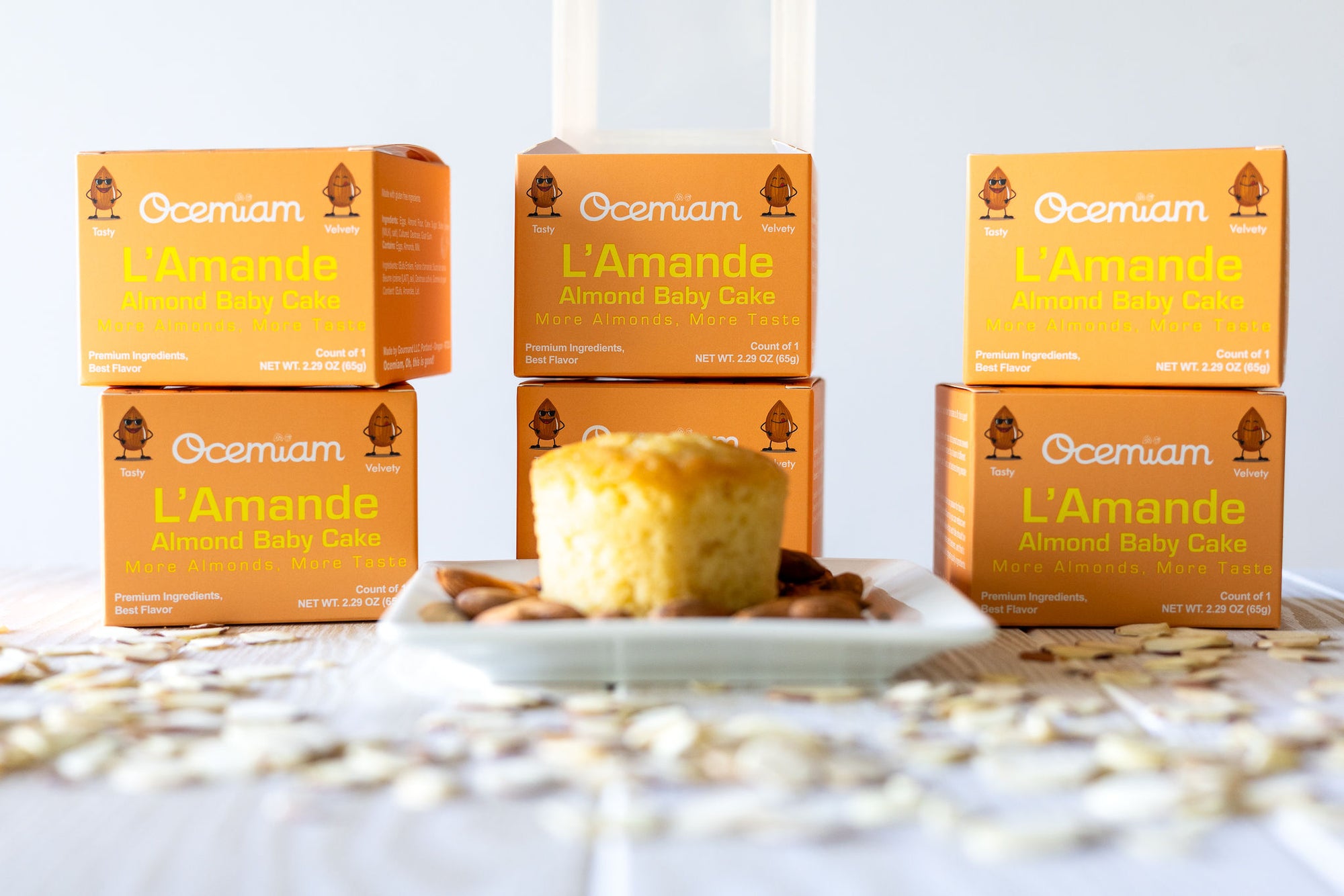 Ocemiam L'Amande almond baby cake boxes with a cake on a white plate.
