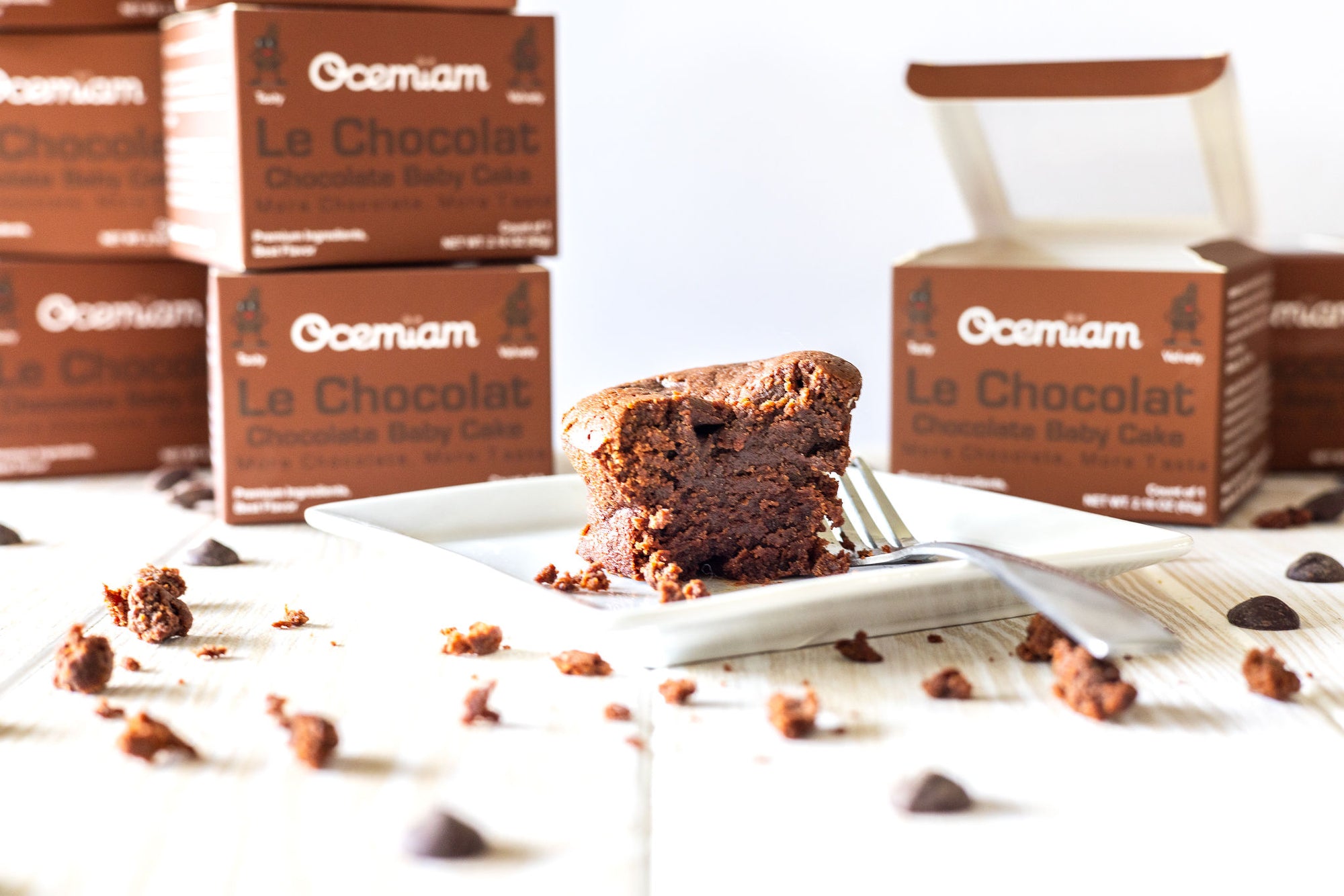 Chocolate cake on a white plate with Ocemian Le Chocolat boxes in the background.
