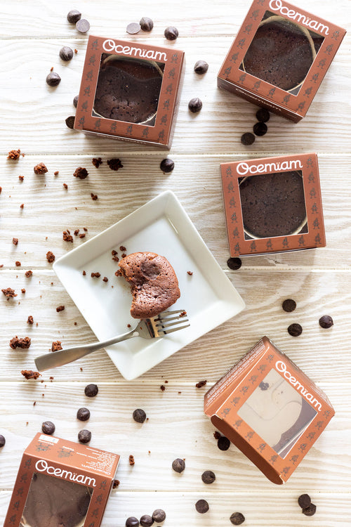 Chocolate cake slices in Ocemiam packaging on a wooden surface with scattered chocolate chips.
