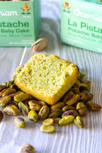 Pistachio cake with pistachios on a wooden surface, with Scrumdilium boxes in the background.
