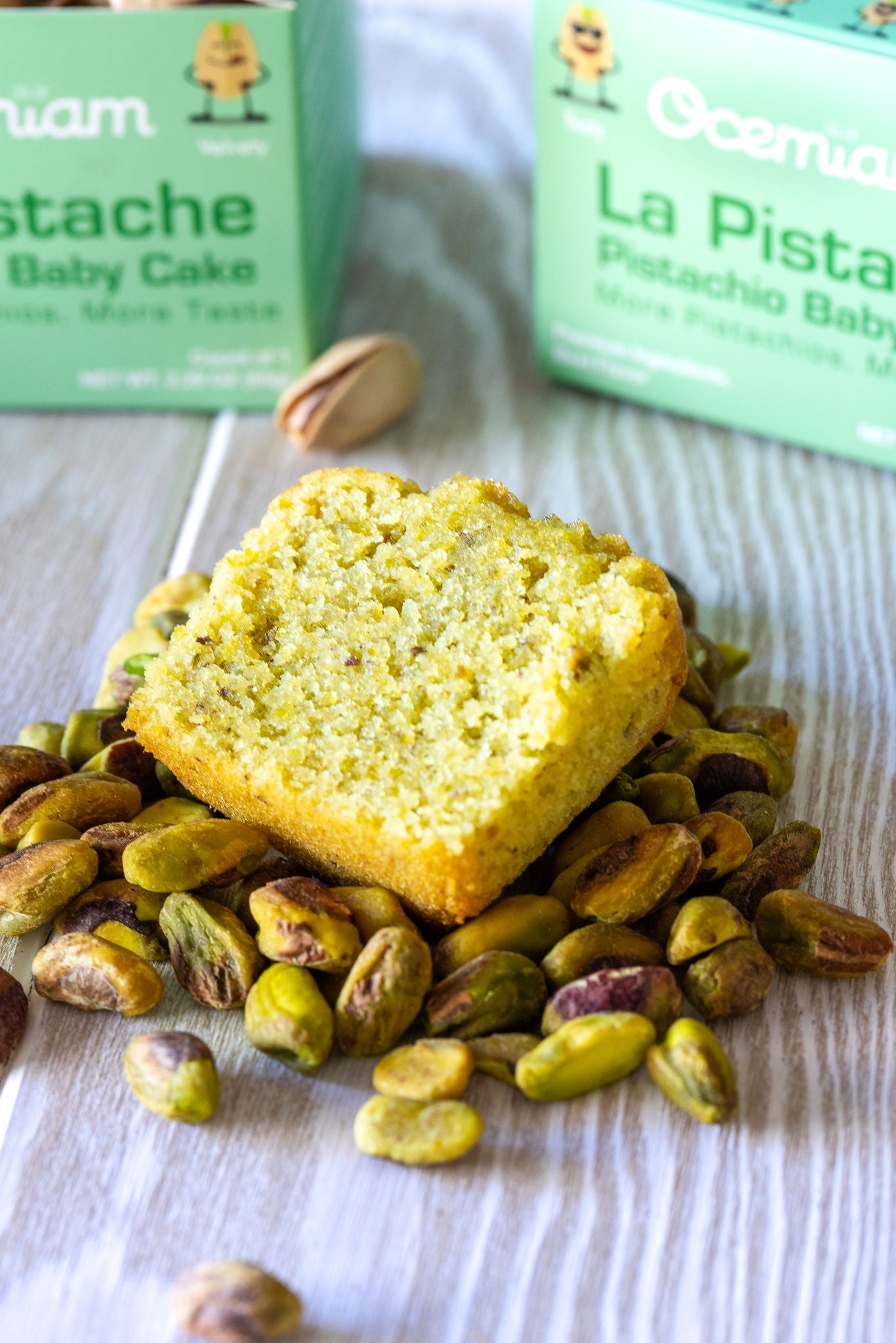 Pistachio cake with pistachios on a wooden surface, with Scrumdilium boxes in the background.