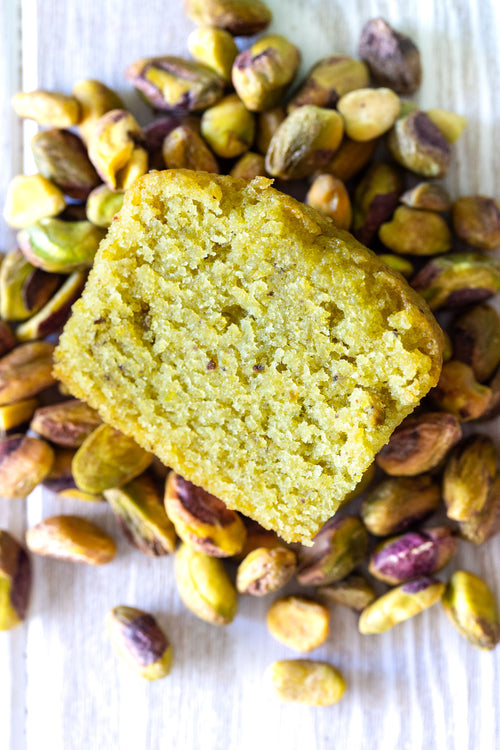 Pistachio cake slice surrounded by pistachios on a white background