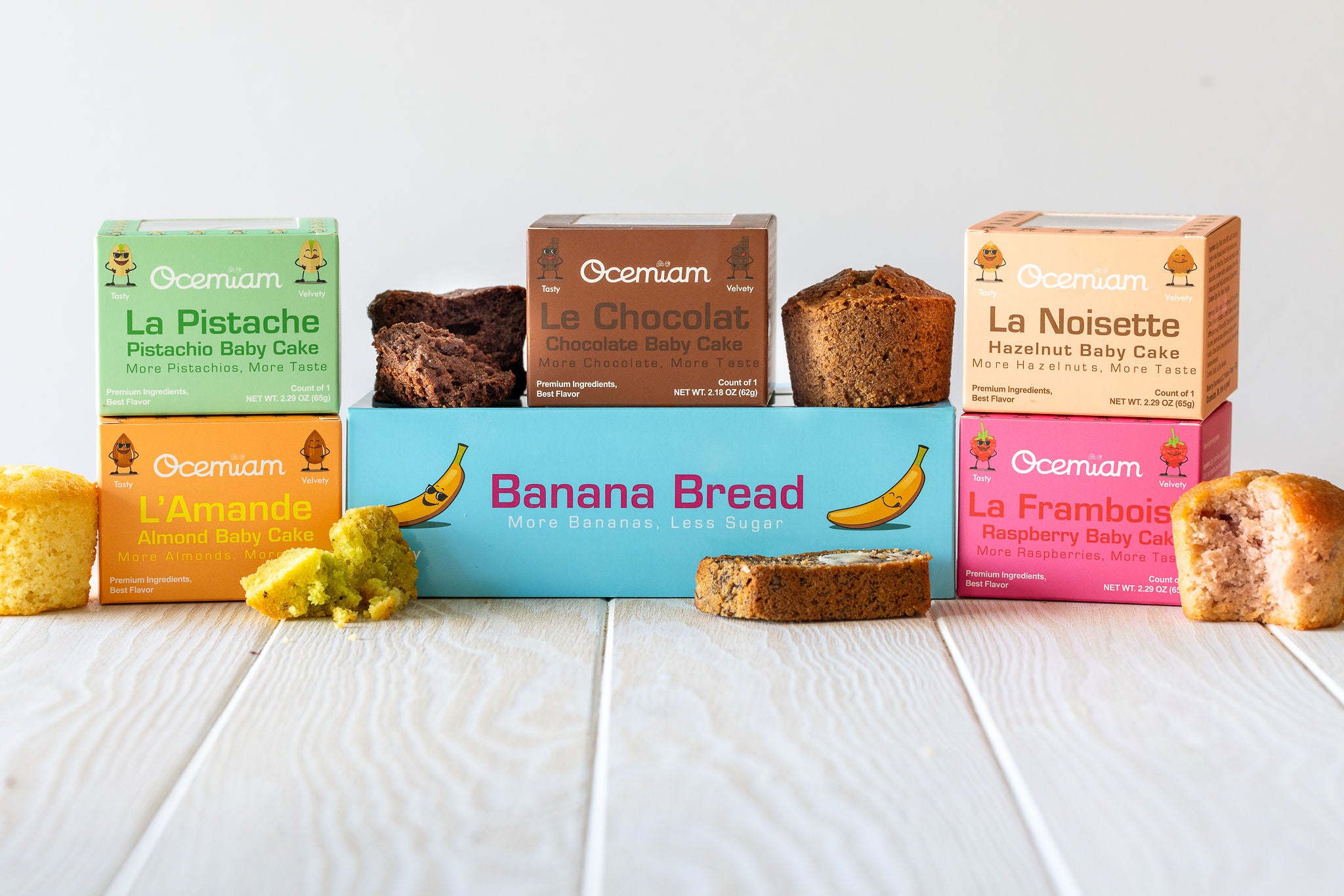 Assorted Ocemiam mini cakes in colorful boxes on a white wooden surface.